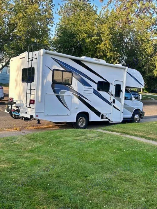 RV rental: A white Class C motorhome with black and silver decals, parked on a sunny day next to a grassy lawn.. Thor Freedom Elite 2021