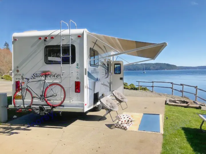 Waterfront rv rental with an extended awning, bicycle, and a cozy outdoor patio overlooking the ocean.. Thor Freedom Elite 2021