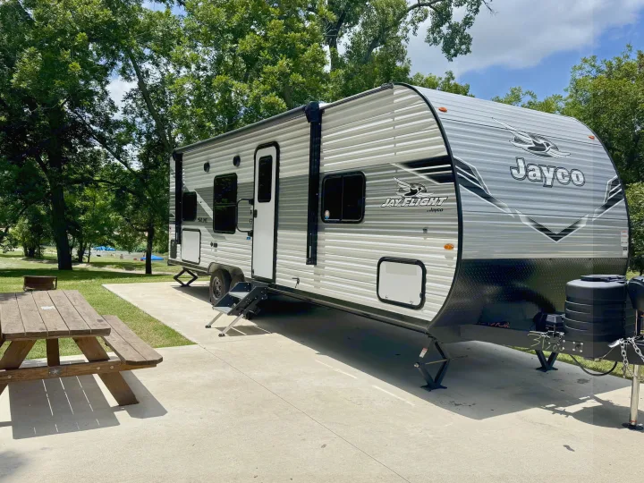 RV rental: A Jayco travel trailer parked at a sunny campsite with a picnic table and trees, near a lake with people.. Jayco 260BH 2026