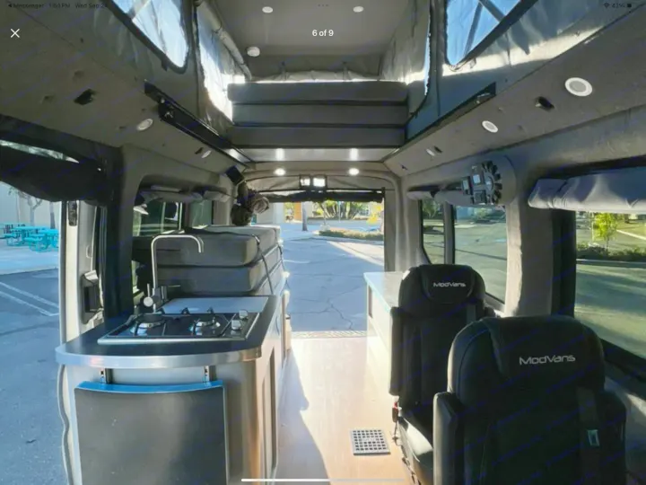 Explore this ModVans rv rental: a cozy camper van interior with a kitchenette, elevated bed, and comfortable rear seating.. ModVans ModVans Class B 2022