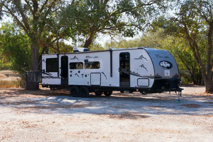 This white and grey "Black Label Grey Wolf" RV rental travel trailer is parked at a sunny campsite for outdoor adventures.. Forest River Black Label 2024