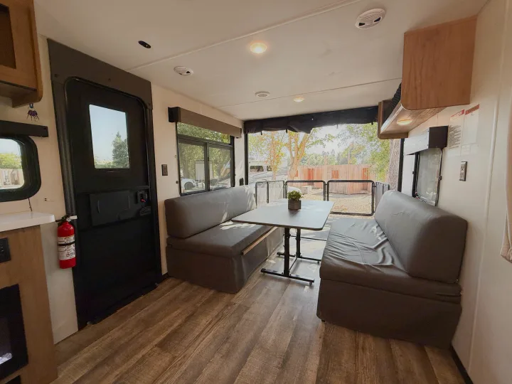 Modern RV rental dining area with cozy benches, wood-style floors, and an open deck view to the outdoors. Ideal for adventures!. Forest River Black Label 2024