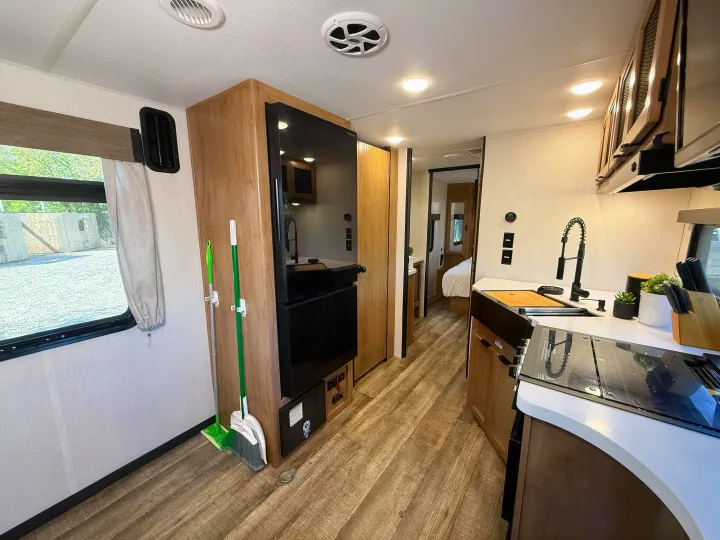 Spacious rv rental interior featuring a full kitchen with modern appliances, a window view, and a hallway to the bedroom.. Forest River Black Label 2024