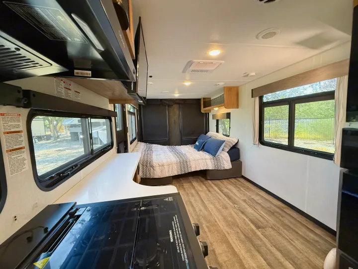 Spacious RV rental interior featuring a cozy bed, modern kitchen with stovetop, and large windows with natural light.. Forest River Black Label 2024