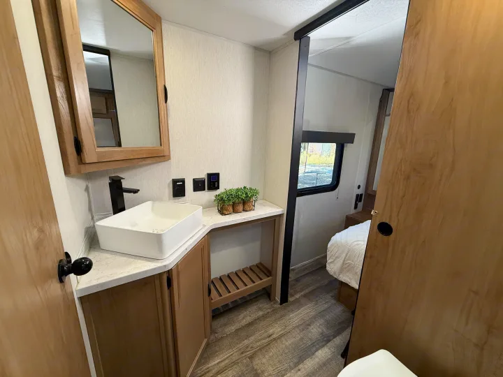 RV rental: Bright bathroom with vessel sink, black faucet, and mirrored cabinet. Sliding door opens to a cozy bedroom. Wood-look flooring.. Forest River Black Label 2024