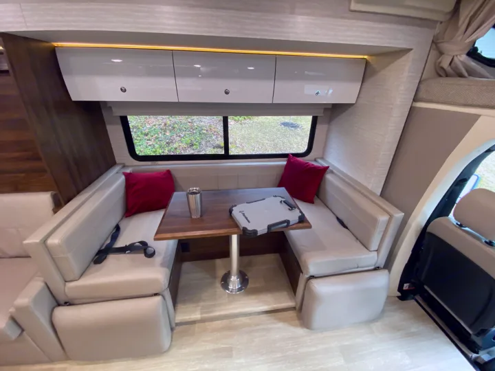 Cozy RV rental dinette with booth seating, table, overhead storage, and windows, a comfortable space for dining and relaxation.. Winnebago View 2020