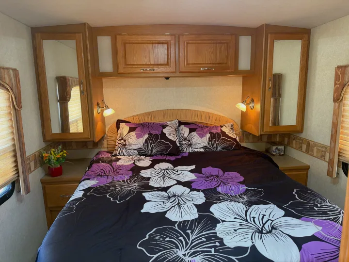 Cozy RV bedroom for your next rv rental adventure, featuring floral bedding, overhead storage, and compact nightstands with reading lights.. Triple E Embassy 2003