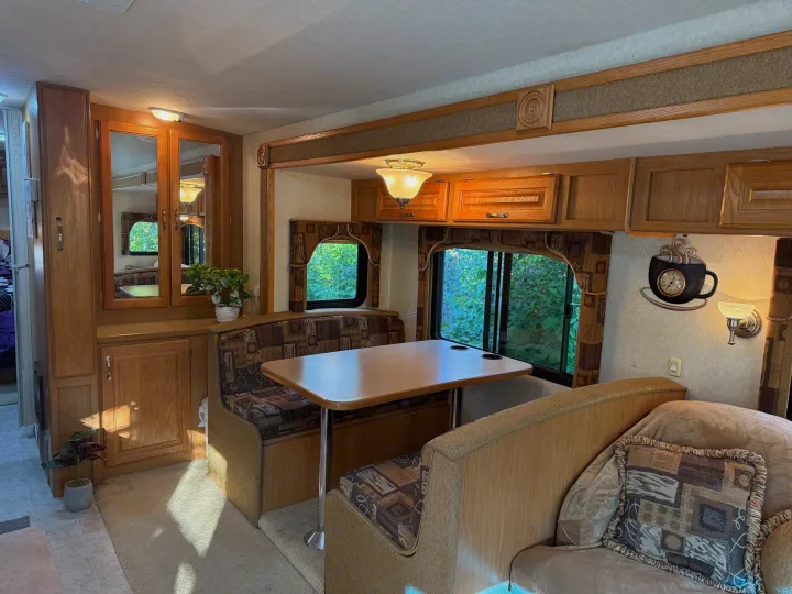 RV rental interior showing a comfortable dinette, wooden cabinetry, and bright windows with lush outdoor views.. Triple E Embassy 2003