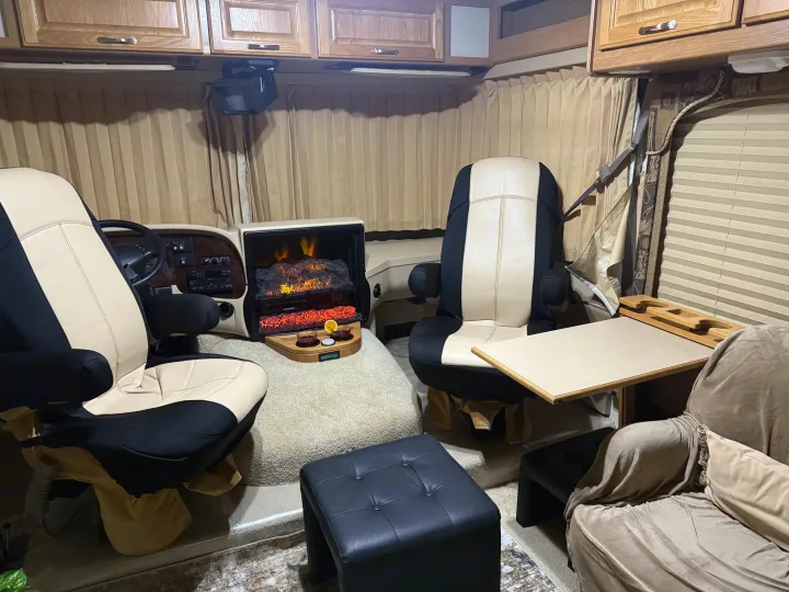 Cozy RV rental living space featuring an electric fireplace, plush captain's chairs, and a comfy armchair, creating a homey atmosphere.. Triple E Embassy 2003
