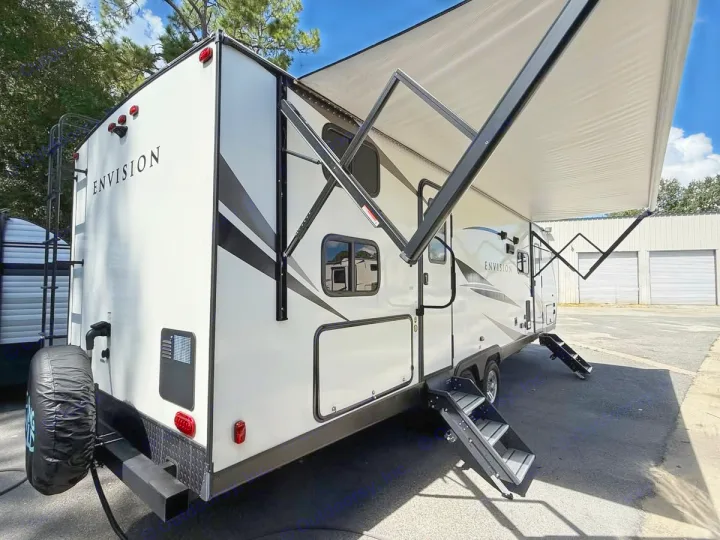 White Envision travel trailer, an ideal rv rental, with extended awning, entry steps, and rear-mounted spare tire, parked outdoors.. Gulf Stream Envision 2023