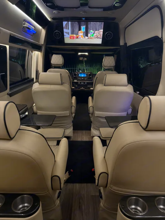 Luxury RV rental interior: spacious cream seats, entertainment screen playing cartoons. Plush comfort for your journey.. Ultimate Toys Ultimate Coach 2023
