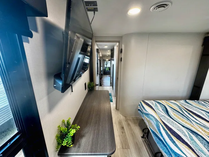 Spacious RV rental bedroom and hallway with a mounted TV and comfortable bed, showcasing modern interior design.. Keystone RV Montana High Country 2024