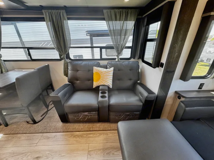 Comfortable RV rental interior: gray reclining seats, yellow pillow, dining area, and large windows with curtains.. Keystone RV Montana High Country 2024