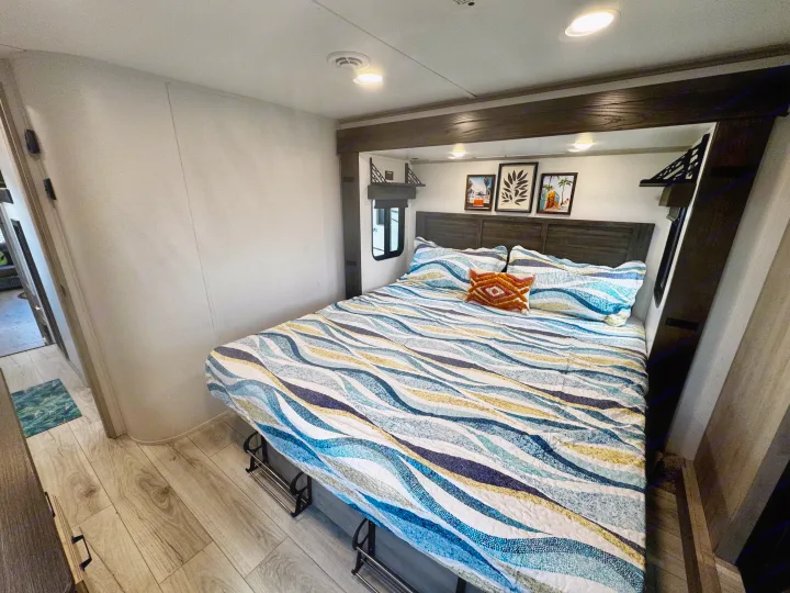 Comfortable RV rental bedroom features a vibrant patterned bed, decorative art, and handy under-bed shoe storage for travel.. Keystone RV Montana High Country 2024
