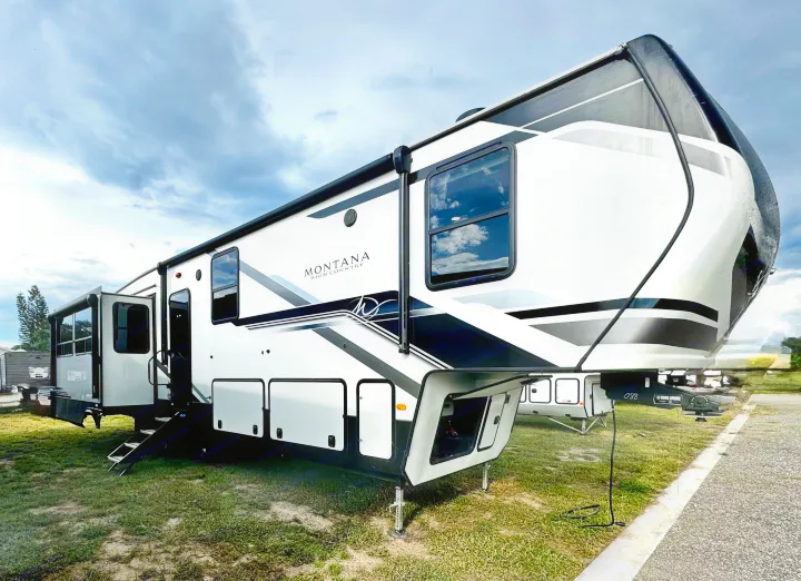 Large white Montana High Country fifth-wheel RV for rv rental, featuring black accents, parked on grass under cloudy skies.. Keystone RV Montana High Country 2024