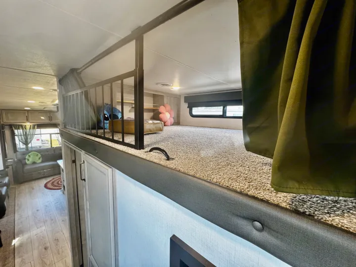 Cozy RV rental features a carpeted loft with railing, stuffed animals, and a spacious living area with a couch below.. Keystone RV Montana High Country 2024