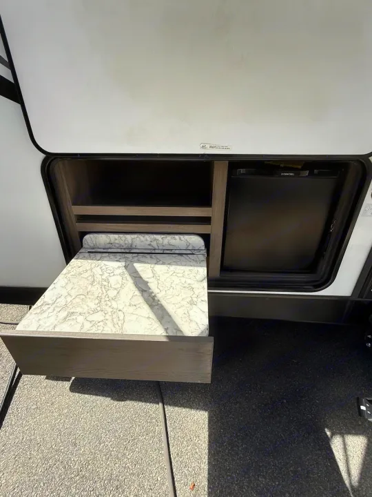 An RV rental's outdoor kitchen features a pull-out counter, storage shelves, and an Ever Chill mini-fridge for convenience.. Gulf Stream Envision 2023