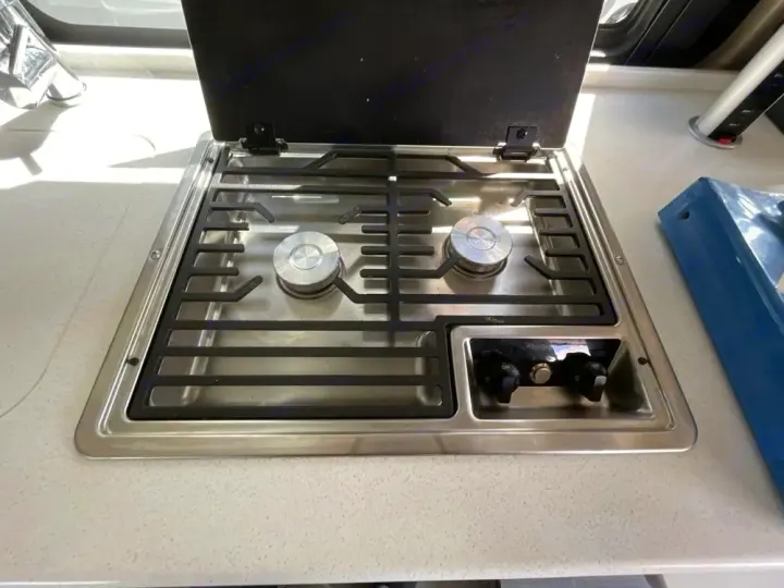 An rv rental kitchen showcases a shiny two-burner gas cooktop with black grates, control knobs, and an open black lid.. Thor Rize 2022