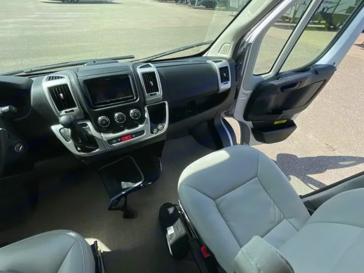 View of an RV rental cockpit: dashboard, infotainment system, gear shifter, and light gray seats.. Thor Rize 2022