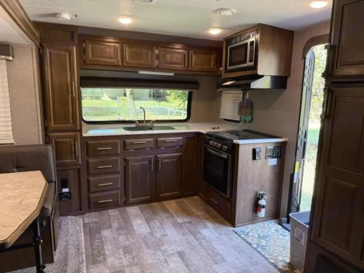 This RV rental offers a well-equipped kitchen with dark wood cabinets, stove, microwave, sink, and dining booth.. Forest River Rockwood Mini Lite 2020