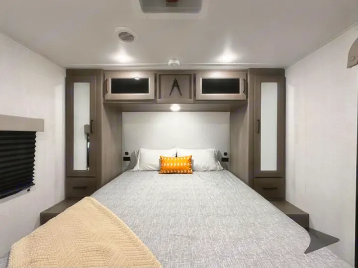 Cozy RV rental bedroom with a comfortable bed, stylish overhead storage, and modern interior lighting.. Grand Design Transcend 2026