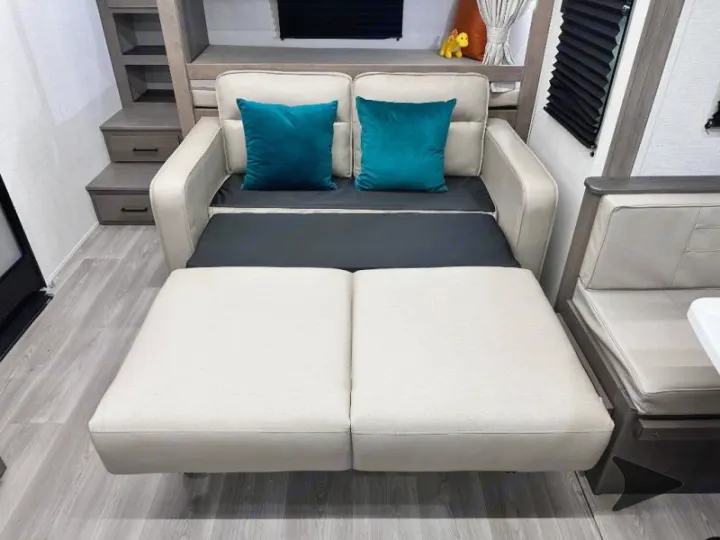 RV rental interior: sofa bed extended for sleeping, featuring beige cushions and teal accents, providing versatile comfort.. Grand Design Transcend 2026