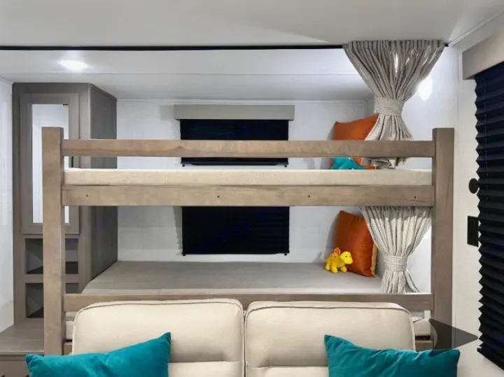 Inside an RV rental: comfortable bunk beds with soft cushions, privacy blinds & curtains, plus a toy dinosaur.. Grand Design Transcend 2026