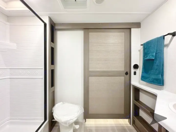 Modern RV rental bathroom interior, showing a tile-patterned shower, covered toilet, and vanity with a blue towel.. Grand Design Transcend 2026