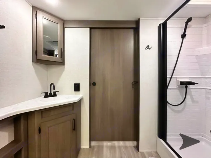 RV rental bathroom: wood vanity with sink, sleek black shower, and private sliding door.. Grand Design Transcend 2026
