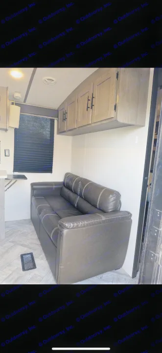 Cozy rv rental interior: black sofa, overhead cabinets, kitchen table, and window with blind. Ideal living space.. Keystone RV Springdale 2022