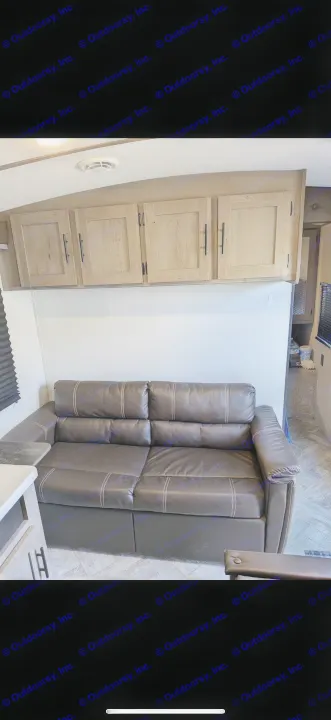 Inside an RV rental: a cozy dark brown sofa, light wood cabinets, and patterned floor, offering comfort on the go.. Keystone RV Springdale 2022