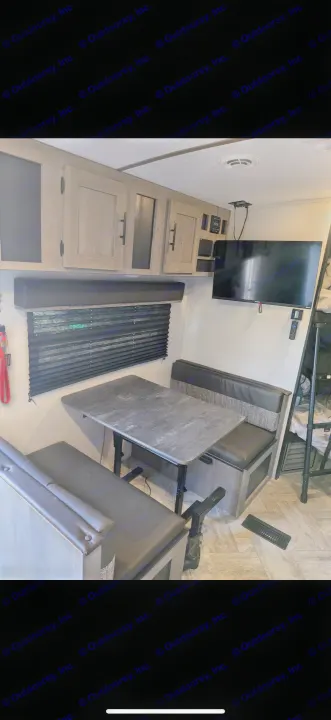 RV rental dinette setup featuring a gray table, cushioned benches, light wood cabinets, and a wall-mounted TV.. Keystone RV Springdale 2022
