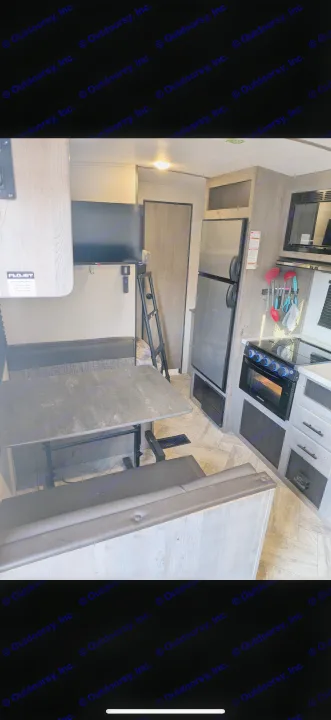 This RV rental's interior boasts a dinette, kitchen with stove, fridge, TV, and a ladder leading to upper bunks.. Keystone RV Springdale 2022
