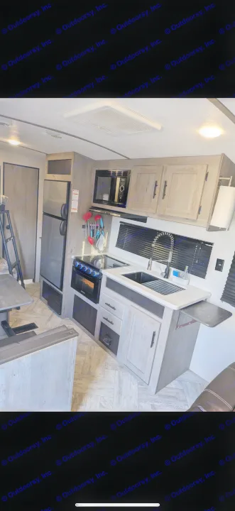 Modern RV rental kitchen with a compact fridge, microwave, stove, sink, and light wood cabinetry for a functional space.. Keystone RV Springdale 2022