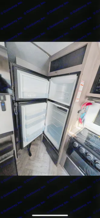 RV rental kitchen: open refrigerator with empty shelves, adjacent stovetop, and TV. Modern, compact interior.. Keystone RV Springdale 2022