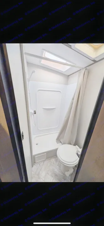 This RV rental features a compact bathroom with a white shower stall, handheld shower, and a toilet. A skylight provides natural light.. Keystone RV Springdale 2022