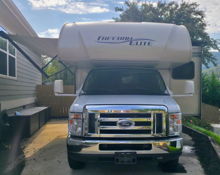 Front view of a white Freedom Elite RV rental, a Ford motorhome parked in a driveway with an awning out. Ready for travel!. Thor Freedom Elite 2019