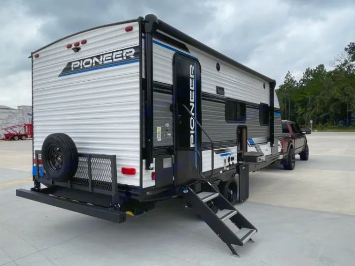 This Pioneer travel trailer, perfect for an RV rental, is hitched to a truck with steps extended & a rear cargo rack.. Heartland RVs Pioneer 2023