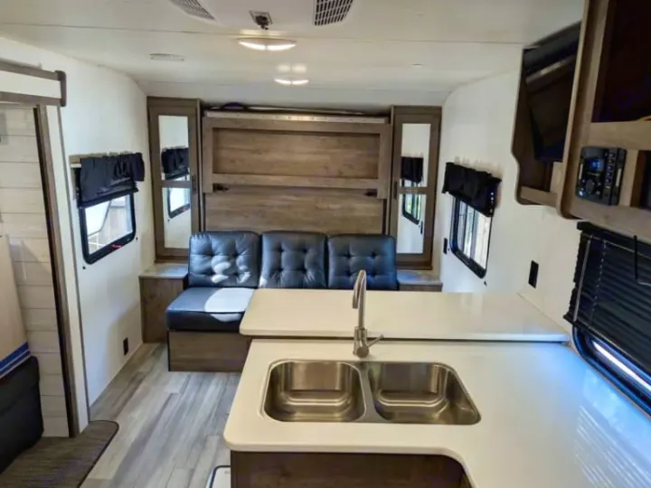 This bright RV rental interior features a kitchen with double sink, comfy seating, and a clever fold-up bed system.. Heartland RVs Pioneer 2023
