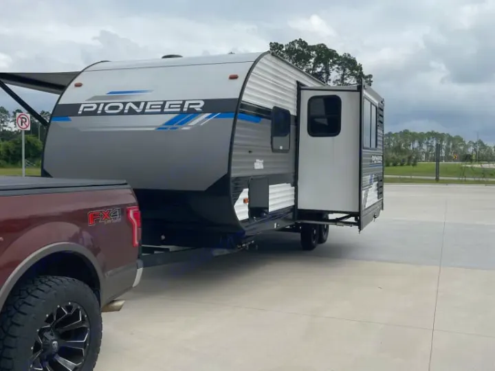 RV rental: A maroon Ford F-150 FX4 tows a gray Pioneer travel trailer, its slide-out extended in a parking lot.. Heartland RVs Pioneer 2023