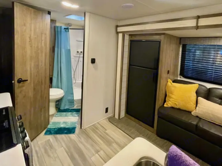 Inside this RV rental: compact bathroom, kitchen with stove, fridge, and living area with a cozy sofa. Road trip ready space.. Heartland RVs Pioneer 2023