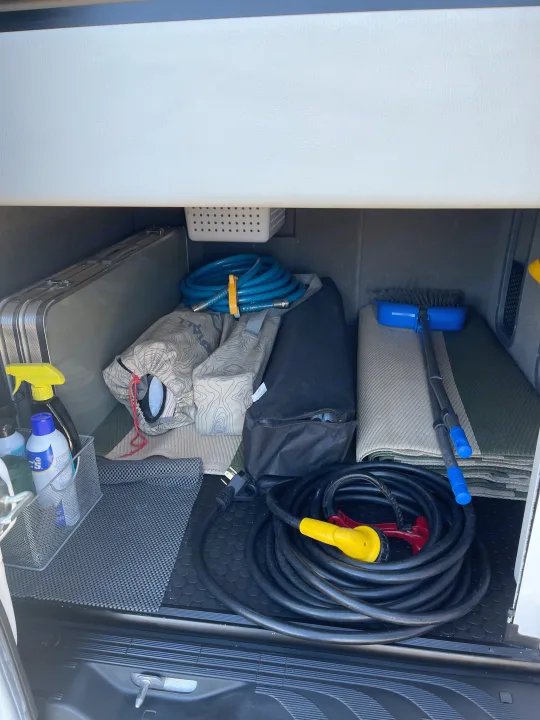 RV rental storage: neatly organized camping gear including power cord, water hose, table, broom, and cleaning supplies.. Coachmen Galleria 2021