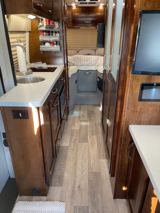 This RV rental interior showcases a compact kitchen, cozy sleeping area, and wood-look floors, perfect for mobile adventures.. Coachmen Galleria 2021