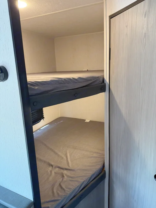 Compact RV rental bunk beds with grey sheets, offering a practical sleep area within a light-toned interior.. Dutchmen Coleman Lantern LT - 274BHWE 2024