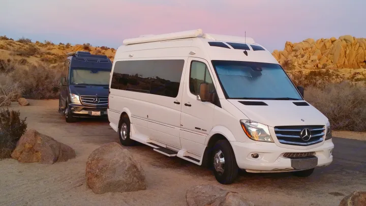 Two Mercedes Sprinter RV rental vans, white and black, parked in a desert landscape at sunset. Ideal for a camper van road trip.. Coachmen Galleria 2020