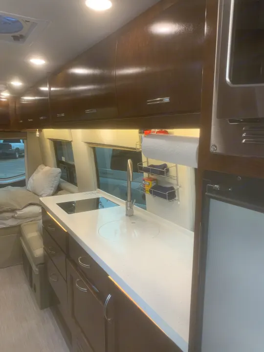 Inside this **rv rental**: a well-equipped compact kitchen with sink, cooktop, and fridge, next to the sleeping area.. Coachmen Galleria 2020