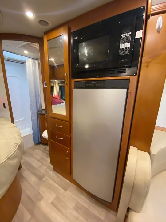 RV rental interior: built-in microwave & refrigerator over wood cabinetry. Behind is a mirror & entrance to the bathroom.. Leisure Travel Van Unity CB 2013
