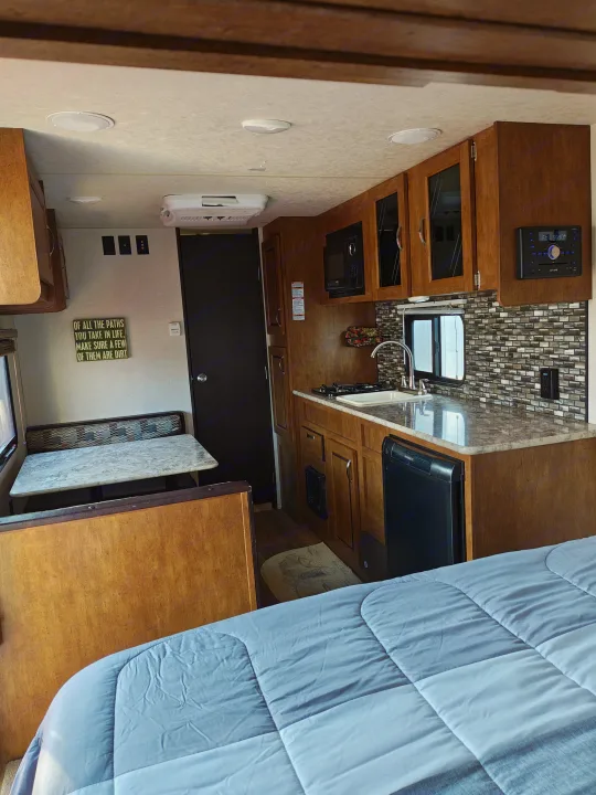 RV rental interior: kitchen with sink, stove, microwave, and fridge; dinette and bed. Wood-toned cabinets for travel.. Forest River Salem FSX 2018