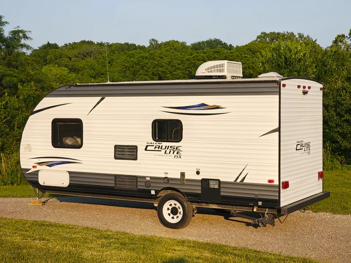 This Salem Cruise Lite travel trailer, a compact RV rental option, is parked on a gravel lot surrounded by green trees.. Forest River Salem FSX 2018