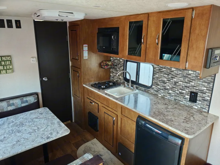 Explore this cozy RV rental interior: a compact kitchen with stove, microwave, sink, and Dometic fridge, plus a dinette.. Forest River Salem FSX 2018